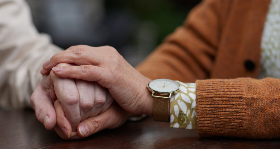 younger hands holding and comforting older hands. Younger hands in foreground wearing a watch.