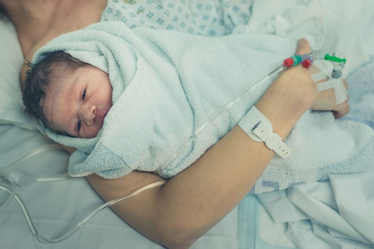 Newborn baby wrapped in a towel, being held in mother's arms on a hospital bed